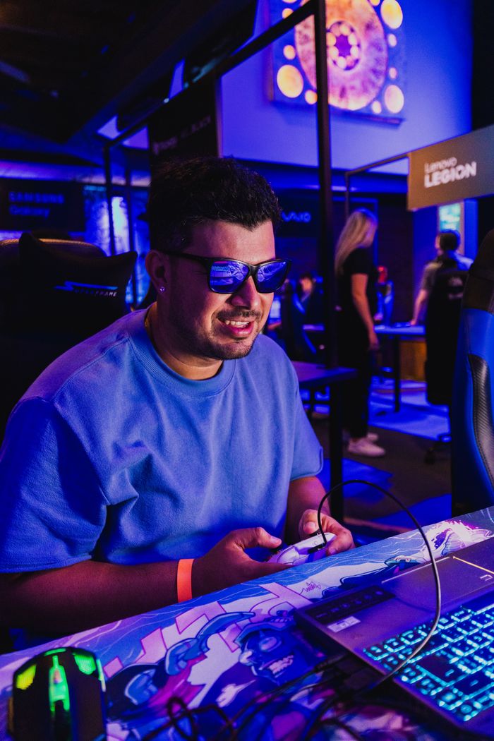 A gamer in sunglasses enjoying a video game at an e-sports event, immersed in action on a laptop.