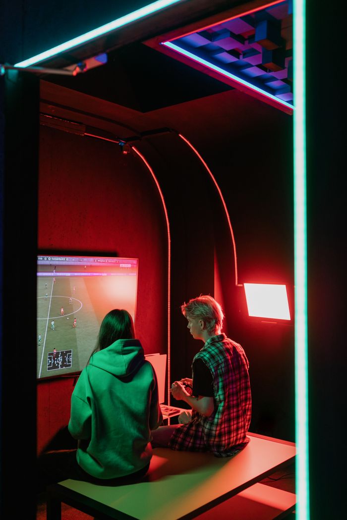 Two young adults playing video games in a neon-lit room, enjoying a gaming session.